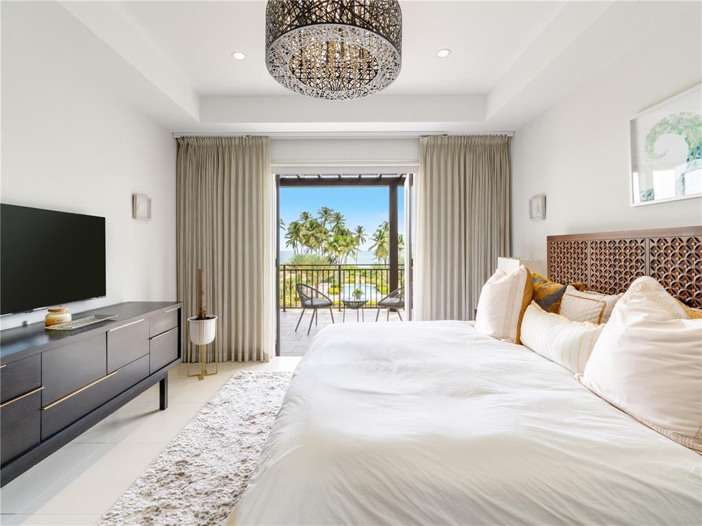 A bedroom features a wooden headboard, a television, and a balcony overlooking palm trees — Ventanas II Condominium 7000 BAHIA BEACH BOULEVARD UNIT 313, RIO GRANDE, PR