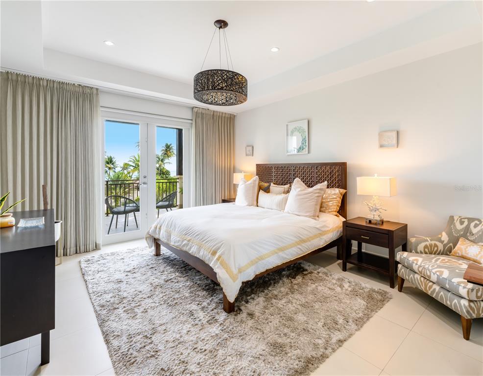A bedroom features a wooden bed, a shag rug, and a balcony with palm trees — Ventanas II Condominium 7000 BAHIA BEACH BOULEVARD UNIT 313, RIO GRANDE, PR