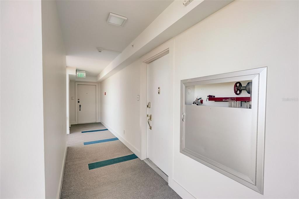 A hallway features gray carpet with blue accents, white walls, and a recessed fire hose cabinet — 2425 GULF OF MEXICO DRIVE UNIT 14B, LONGBOAT KEY, FL