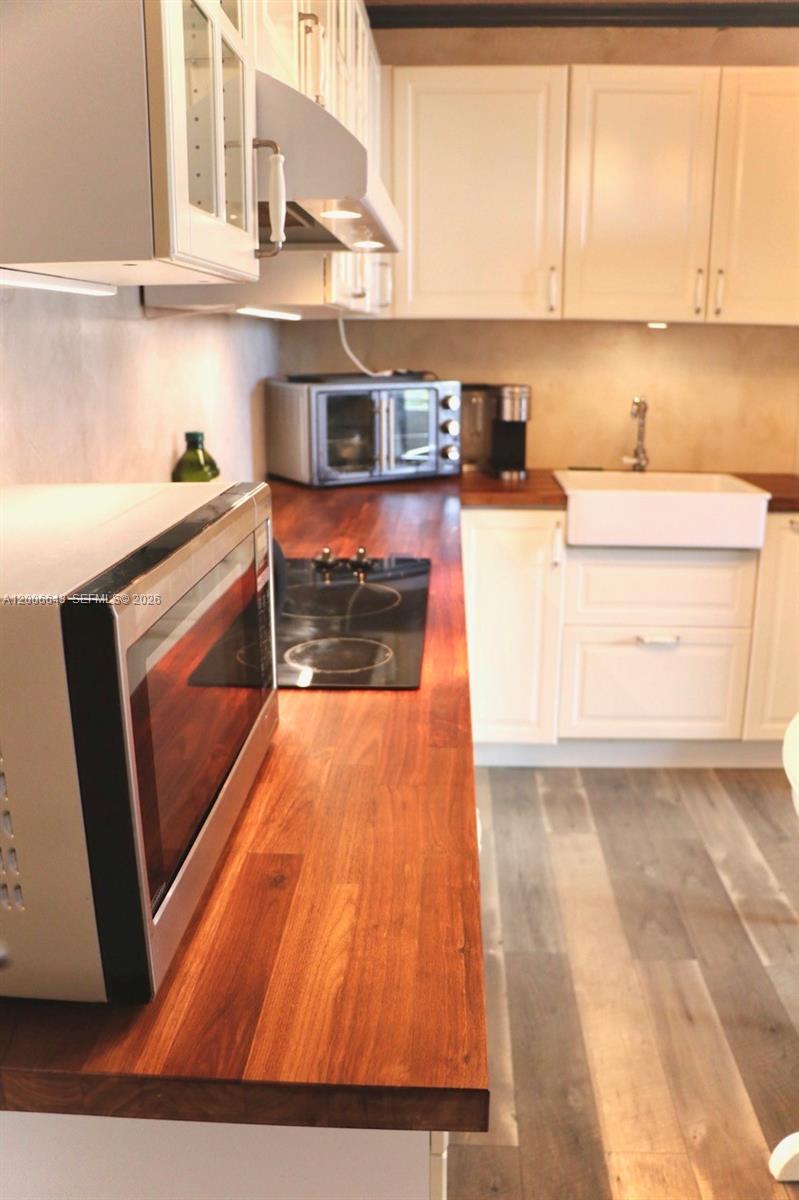 A kitchen features white cabinets, a wood countertop, a stovetop, and a farmhouse sink — HALLANDALE BEACH, FL