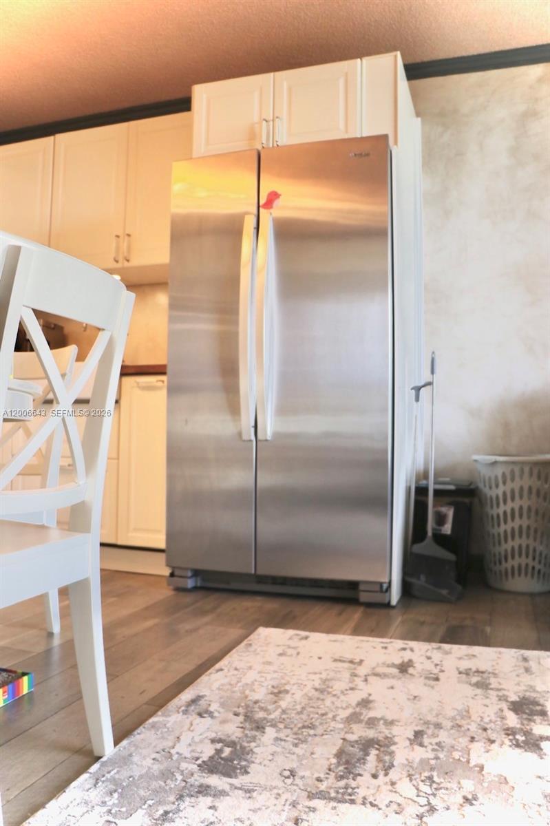 A stainless steel side-by-side refrigerator stands next to white kitchen cabinets and a laundry basket — HALLANDALE BEACH, FL