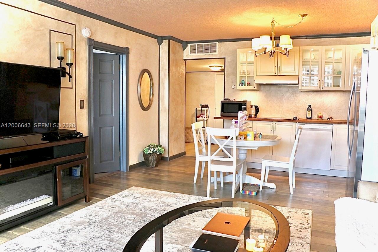 A living room with wood-look flooring flows into a dining area and kitchen with white cabinets — HALLANDALE BEACH, FL