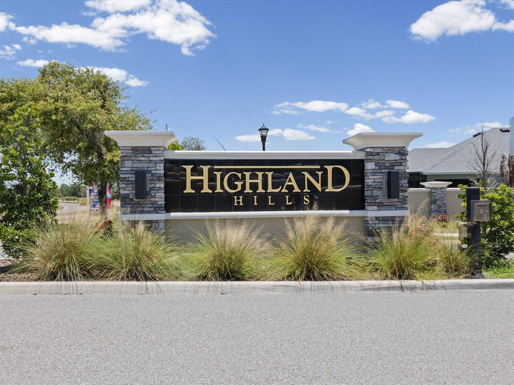 A stone and stucco monument sign for Highland Hills stands beside a paved road — 9401 HIGHLAND HILLS DRIVE, HUDSON, FL