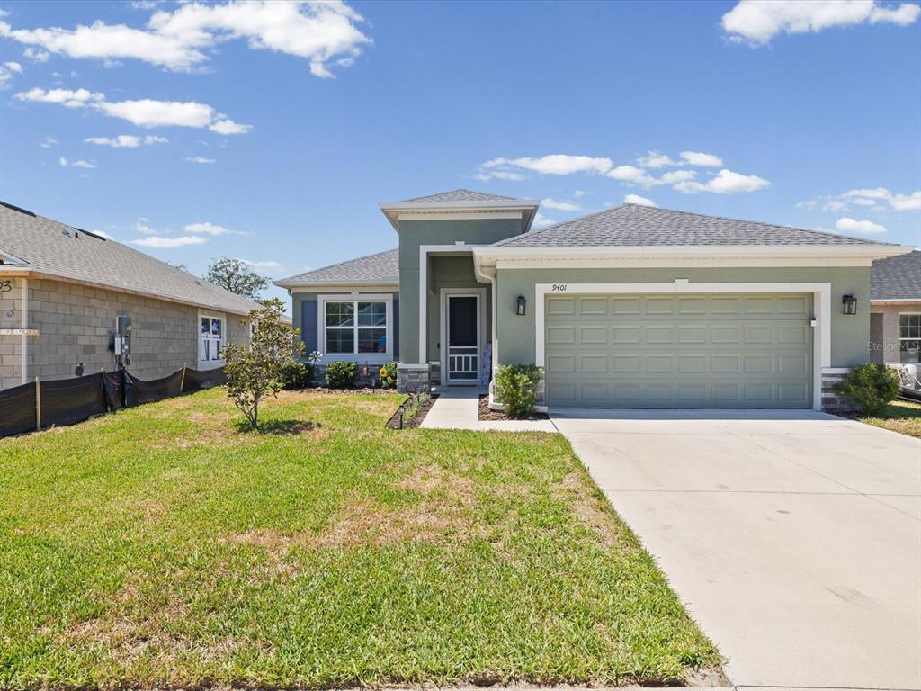 A single-story house with a sage green exterior, a two-car garage, and a front lawn — 9401 HIGHLAND HILLS DRIVE, HUDSON, FL