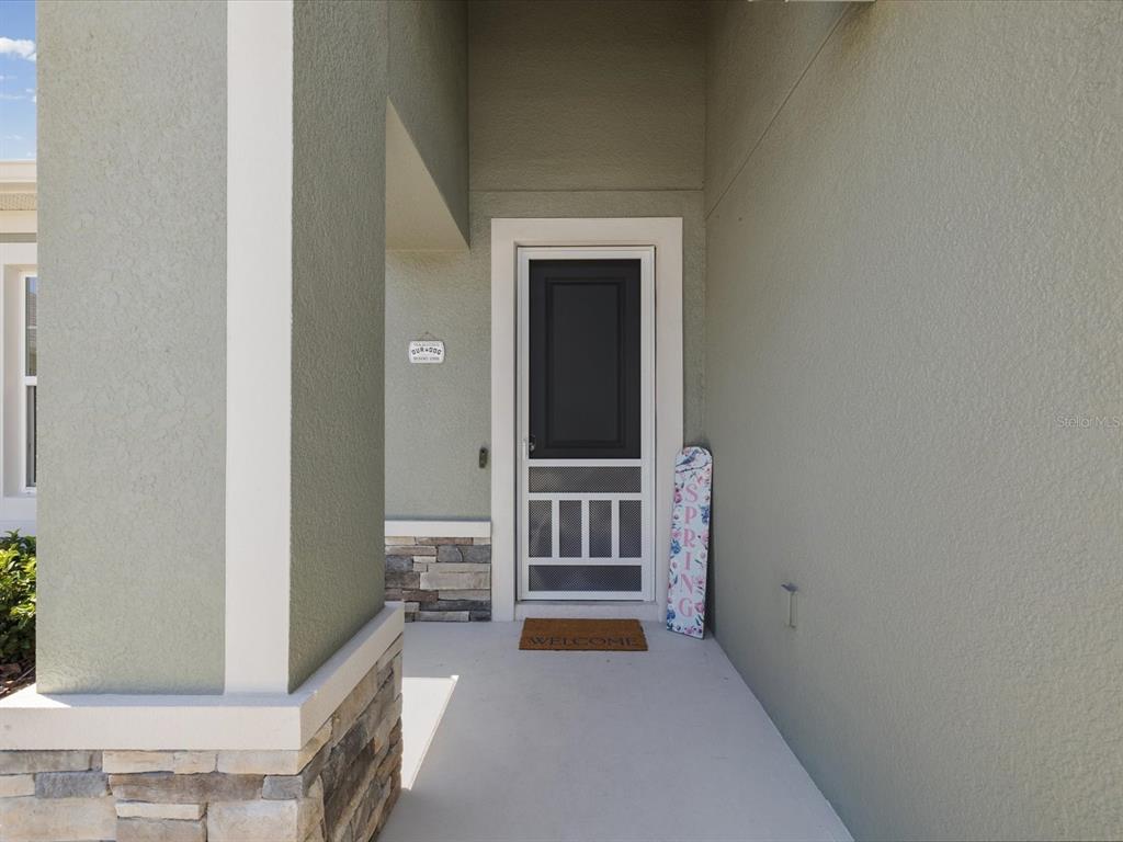 A covered entryway features a light green exterior, a storm door, and a stone base — 9401 HIGHLAND HILLS DRIVE, HUDSON, FL
