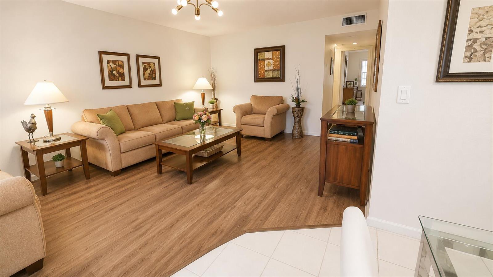 A living room features a beige sofa, armchair, wood-look flooring, and a glass-topped coffee table — 280 Suffolk G, Boca Raton FL 33434, BOCA RATON, FL