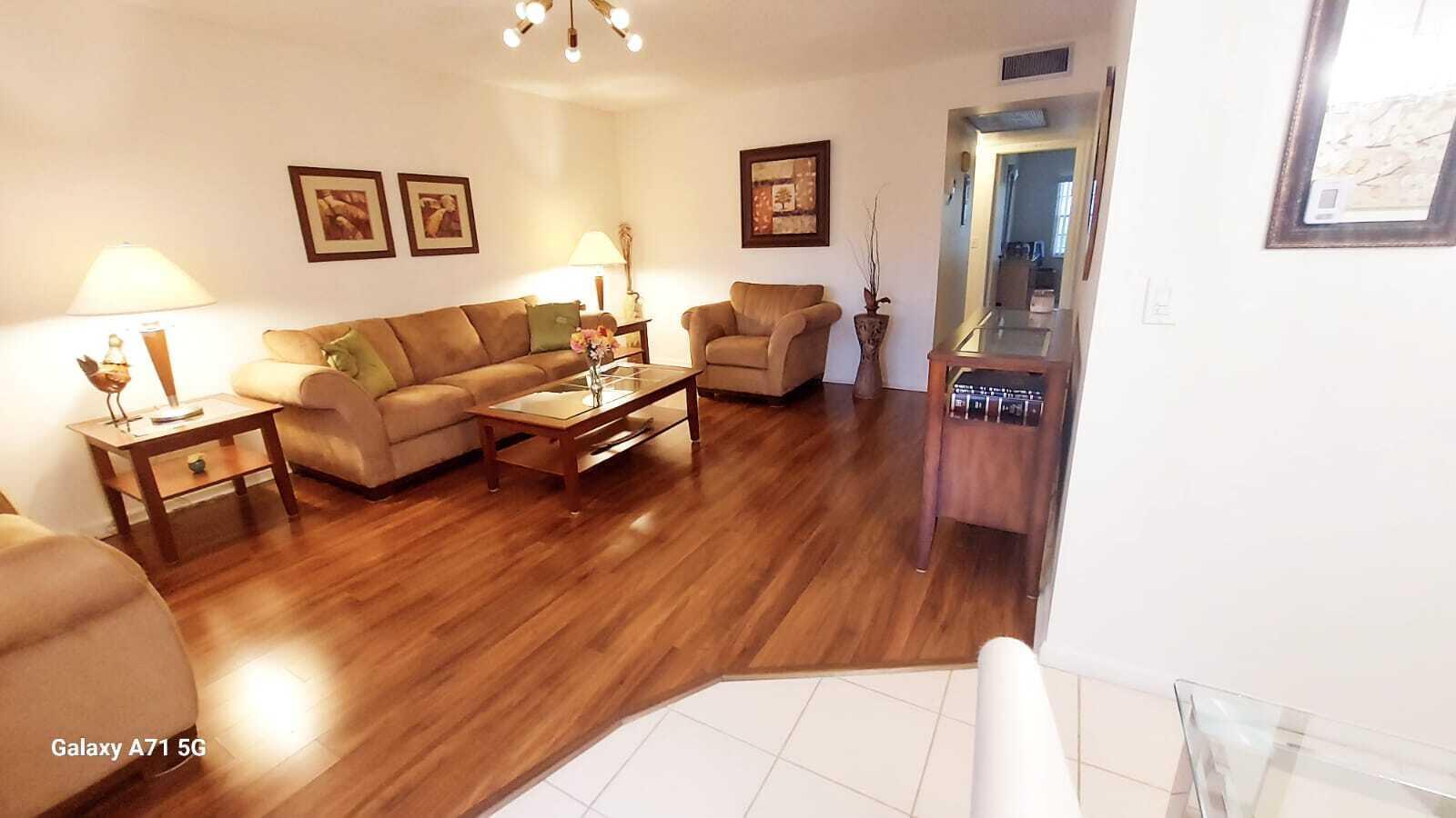 A living room features hardwood floors, a tan sofa, an armchair, and a coffee table — 280 Suffolk G, Boca Raton FL 33434, BOCA RATON, FL