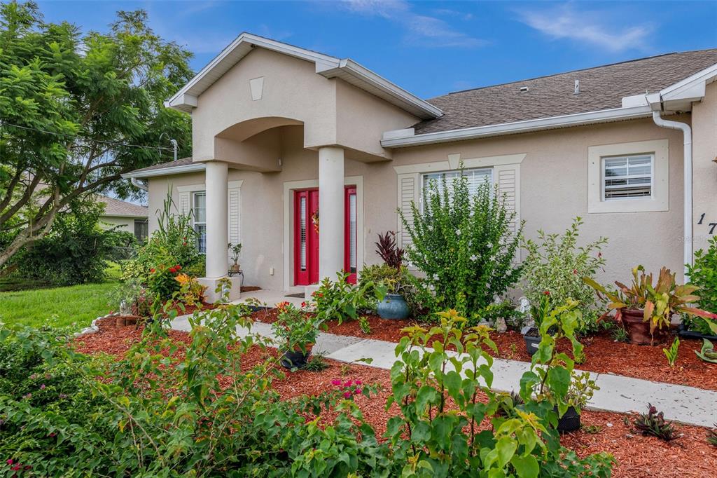 A beige house exterior features a covered entryway with white columns and red double doors — 1751 WALTRIP STREET, NORTH PORT, FL