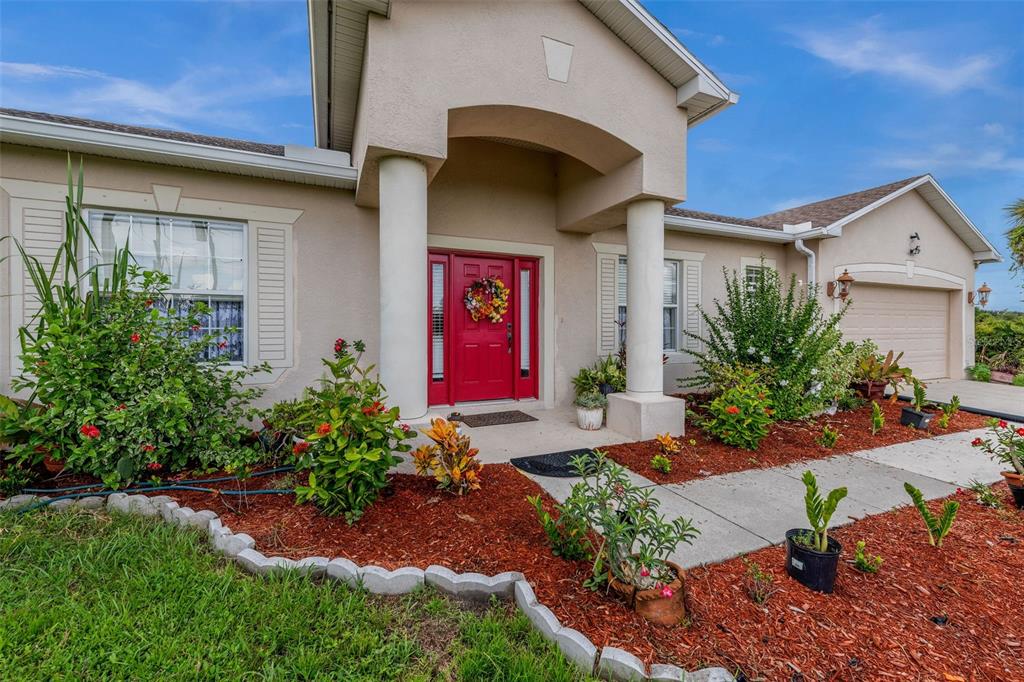 A single-story house with a red front door, two white columns, and landscaped front yard — 1751 WALTRIP STREET, NORTH PORT, FL