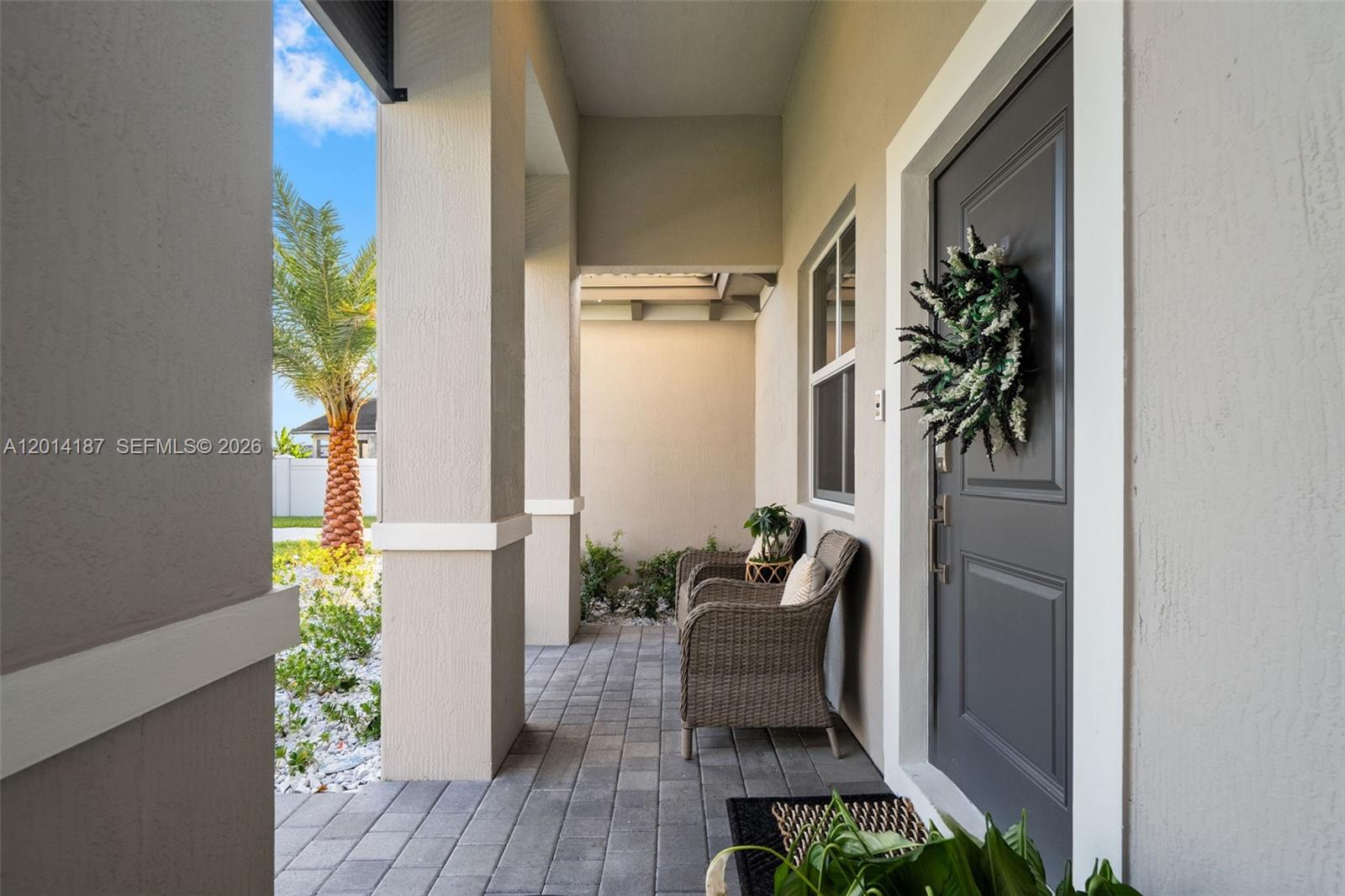 A covered front porch features gray paver flooring, two wicker chairs, and a dark door — 13283 SW 188th Ter, Miami FL 33177, MIAMI, FL