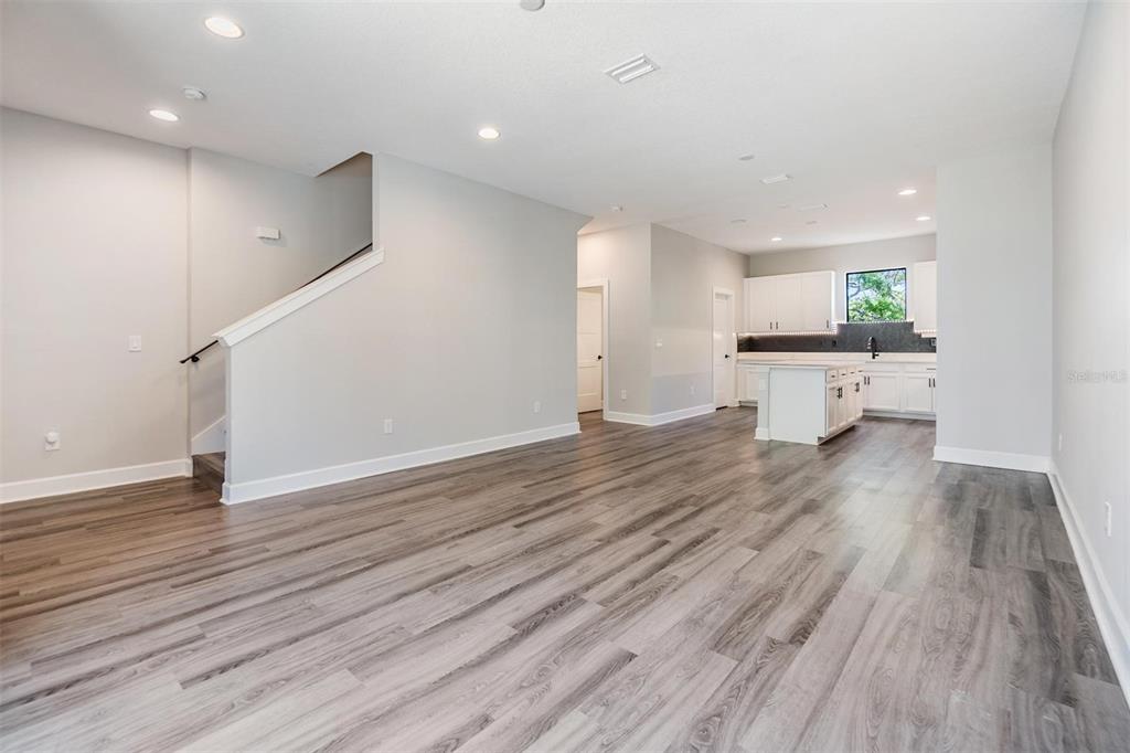 An open-concept living area with light gray walls, wood-look flooring, and a kitchen in back — 1302 W CARMEN STREET UNIT 1, TAMPA, FL