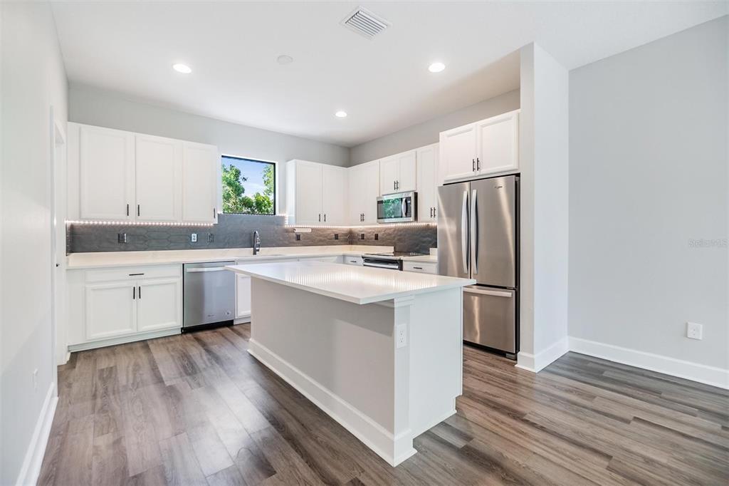 A modern kitchen features white cabinets, stainless steel appliances, a center island, and wood-look flooring — 1302 W CARMEN STREET UNIT 1, TAMPA, FL