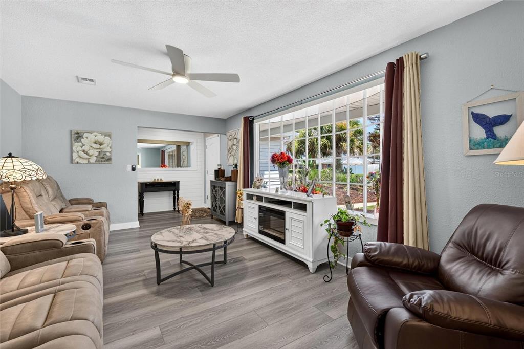 A living room features light gray walls, wood-look flooring, a ceiling fan, and large windows — 117 ANN RUSTIN DRIVE, ORMOND BEACH, FL