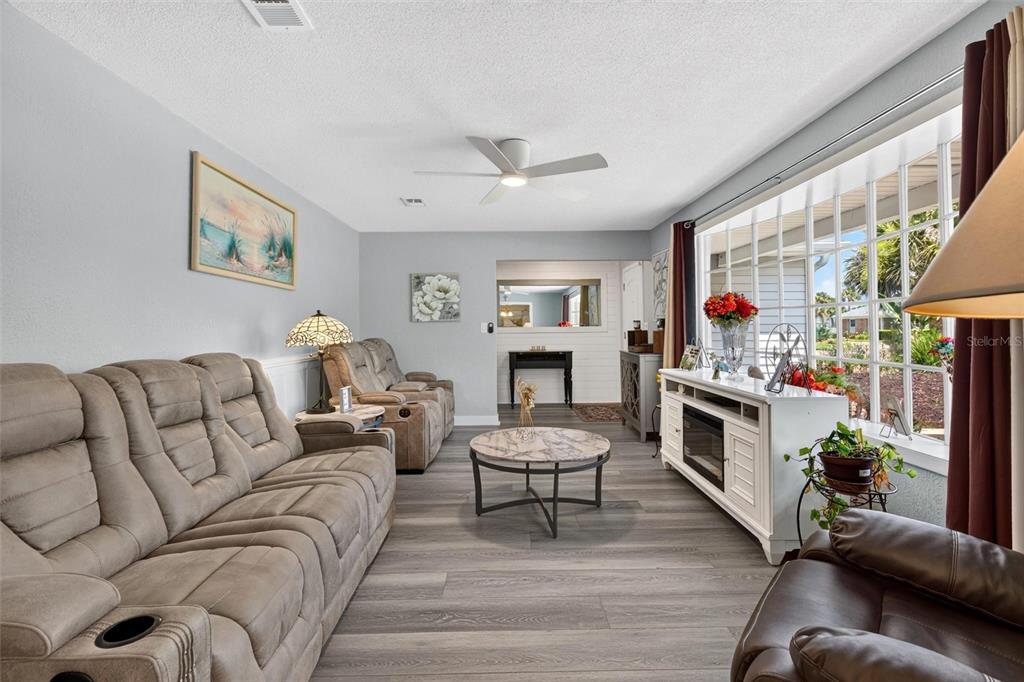 A living room features gray wood-look flooring, a large window, and several brown reclining chairs — 117 ANN RUSTIN DRIVE, ORMOND BEACH, FL