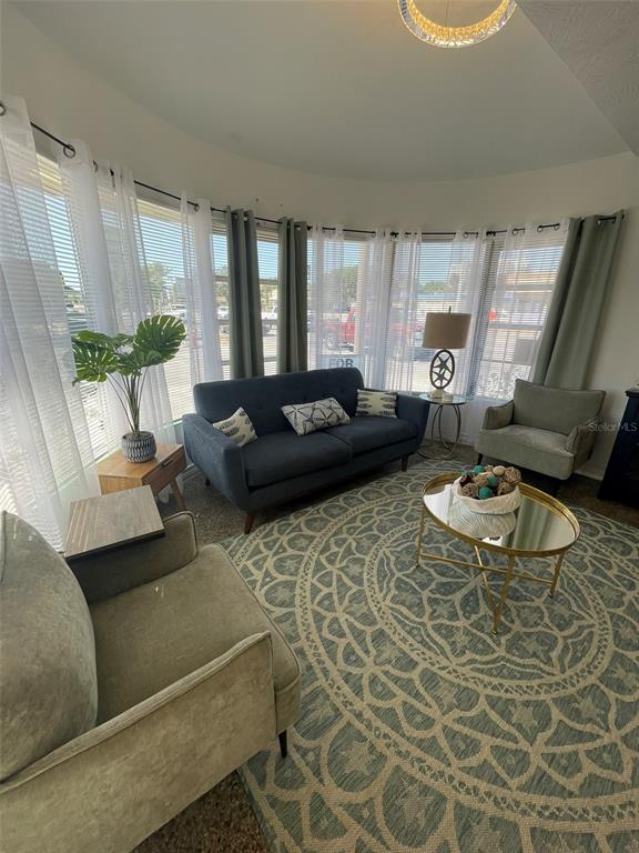 A living room features a curved window wall, a dark sofa, two armchairs, and a rug — 128 RIDGEWOOD AVENUE, DAYTONA BEACH, FL