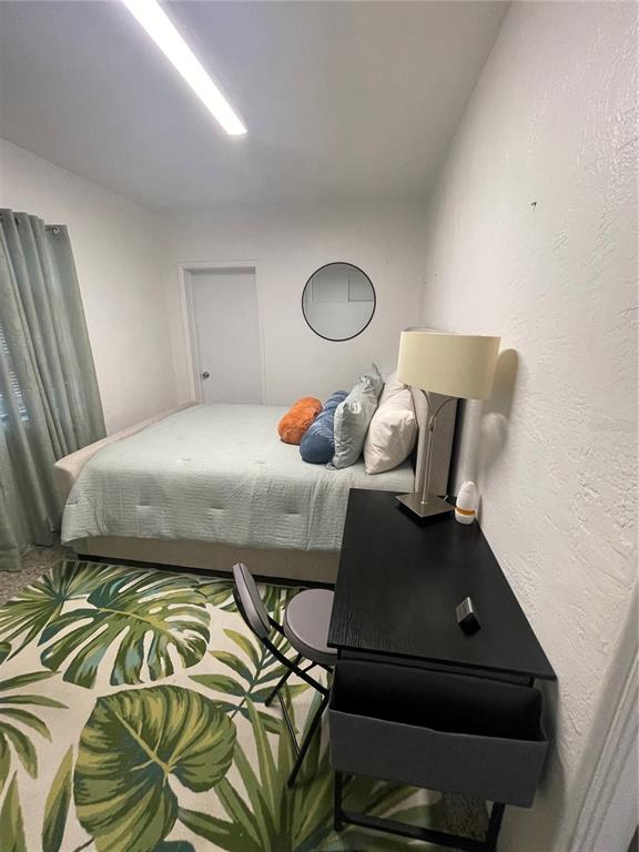 A bedroom features a bed with light bedding, a desk, and a tropical-patterned area rug — 128 RIDGEWOOD AVENUE, DAYTONA BEACH, FL