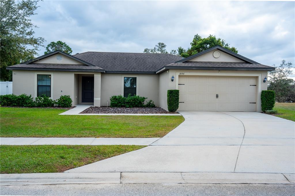 A single-story house with a beige stucco exterior, a two-car garage, and a dark roof — 1896 PIEDMONT COURT, MASCOTTE, FL