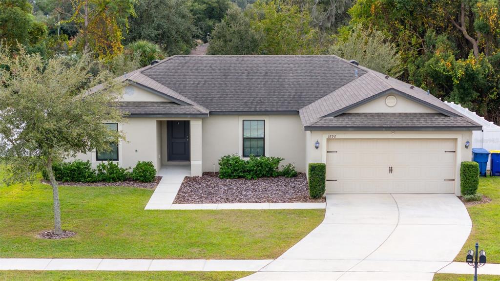 A single-story house with a beige stucco exterior, a two-car garage, and a landscaped front yard — 1896 PIEDMONT COURT, MASCOTTE, FL