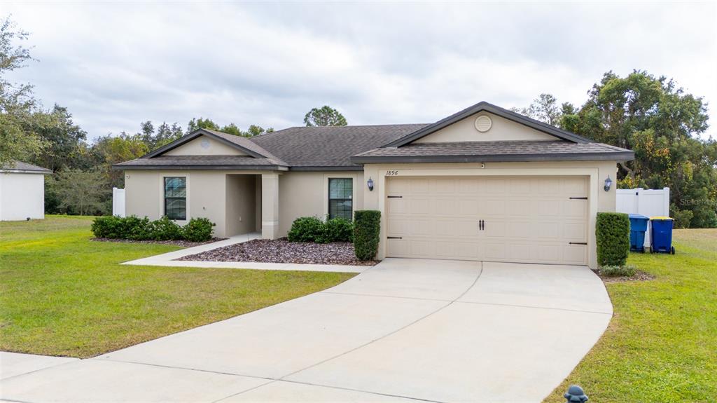 A single-story house with a beige exterior, a two-car garage, and a concrete driveway — 1896 PIEDMONT COURT, MASCOTTE, FL