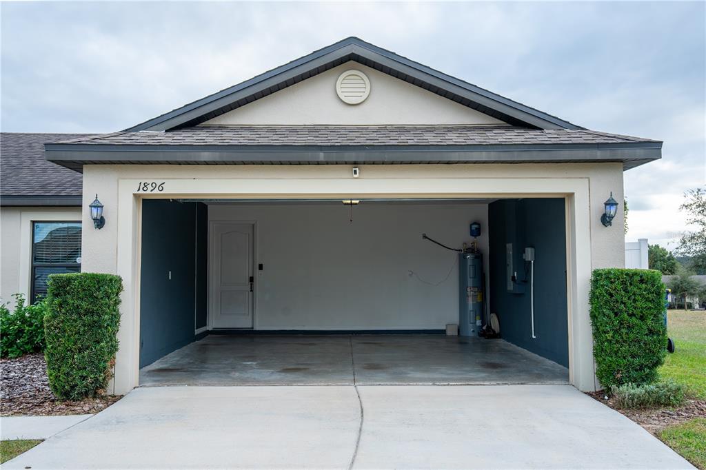 An open garage with a concrete floor, a water heater, and a side entry door — 1896 PIEDMONT COURT, MASCOTTE, FL