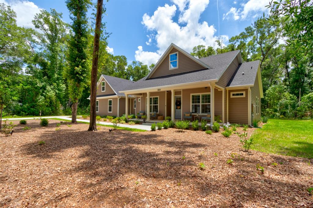 A tan-sided house with a dark shingled roof sits in a wooded, landscaped yard — 3504 DUNSTABLE DRIVE, DELAND, FL