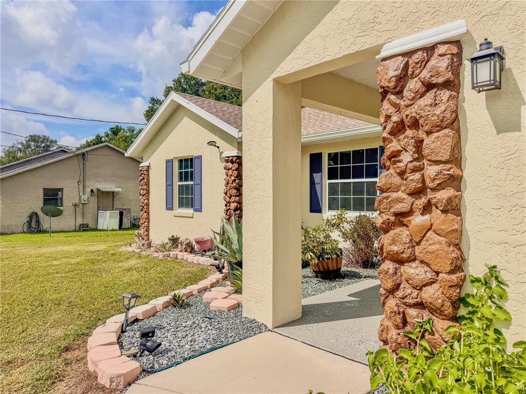 A stone-accented porch leads to the front entrance of a yellow stucco house — 4380 NE 19TH AVENUE, OCALA, FL