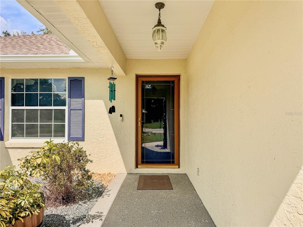 A front entryway features a glass storm door, a hanging light fixture, and blue shutters — 4380 NE 19TH AVENUE, OCALA, FL