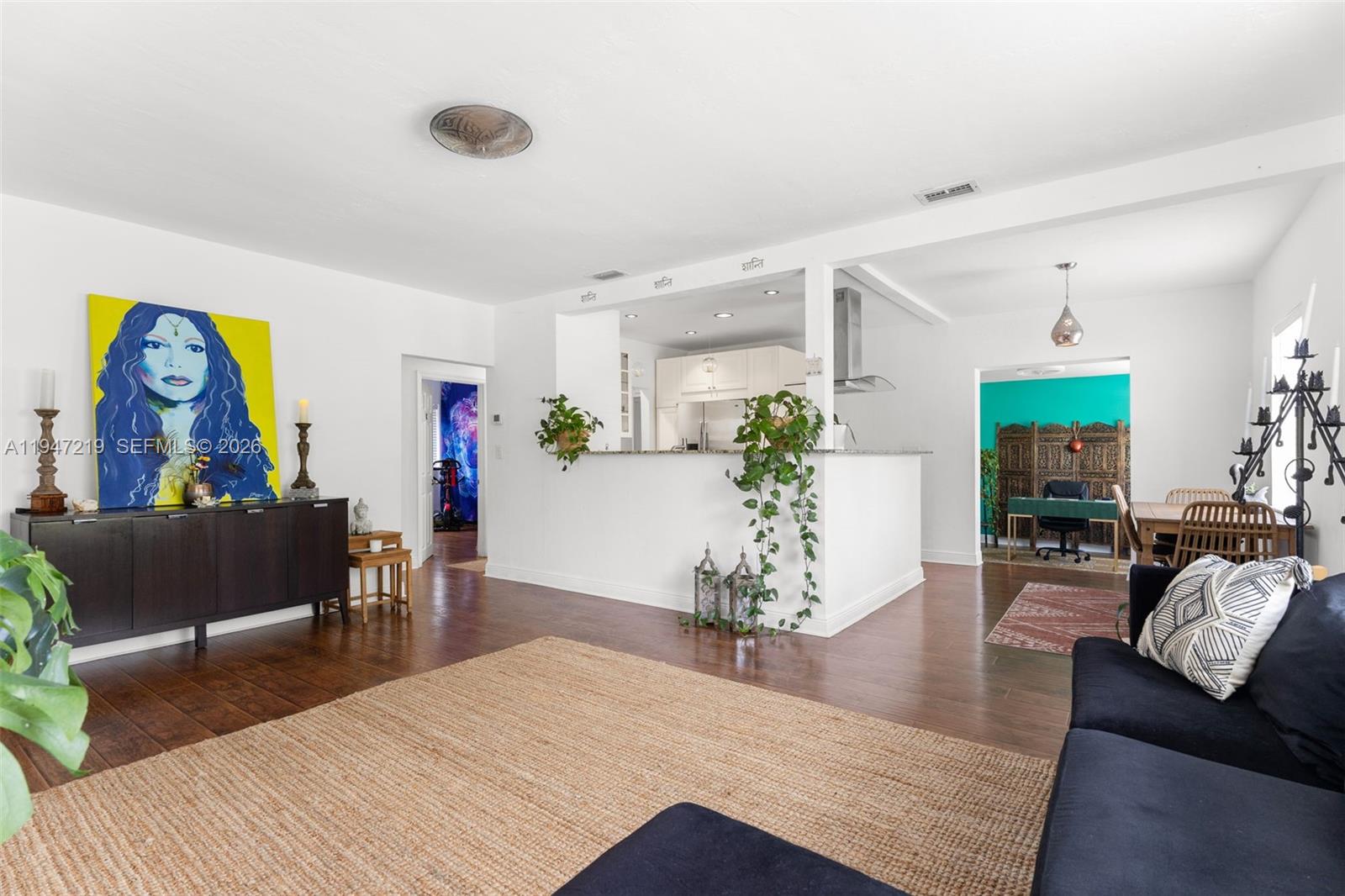 A living room with hardwood floors, a large painting, and an open kitchen area — 550 Cardinal St, Miami Springs FL 33166, MIAMI SPRINGS, FL