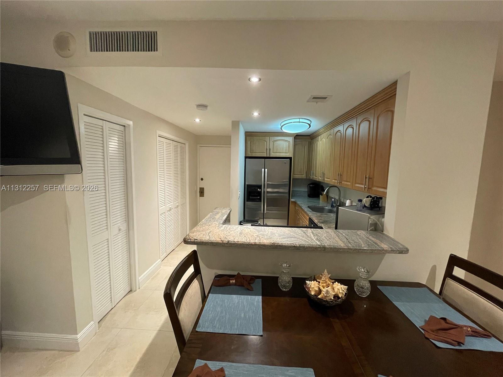 A kitchen with wood cabinets and granite countertops overlooks a dining area with a table — 3505 S Ocean Dr # 108, Hollywood FL 33019, HOLLYWOOD, FL