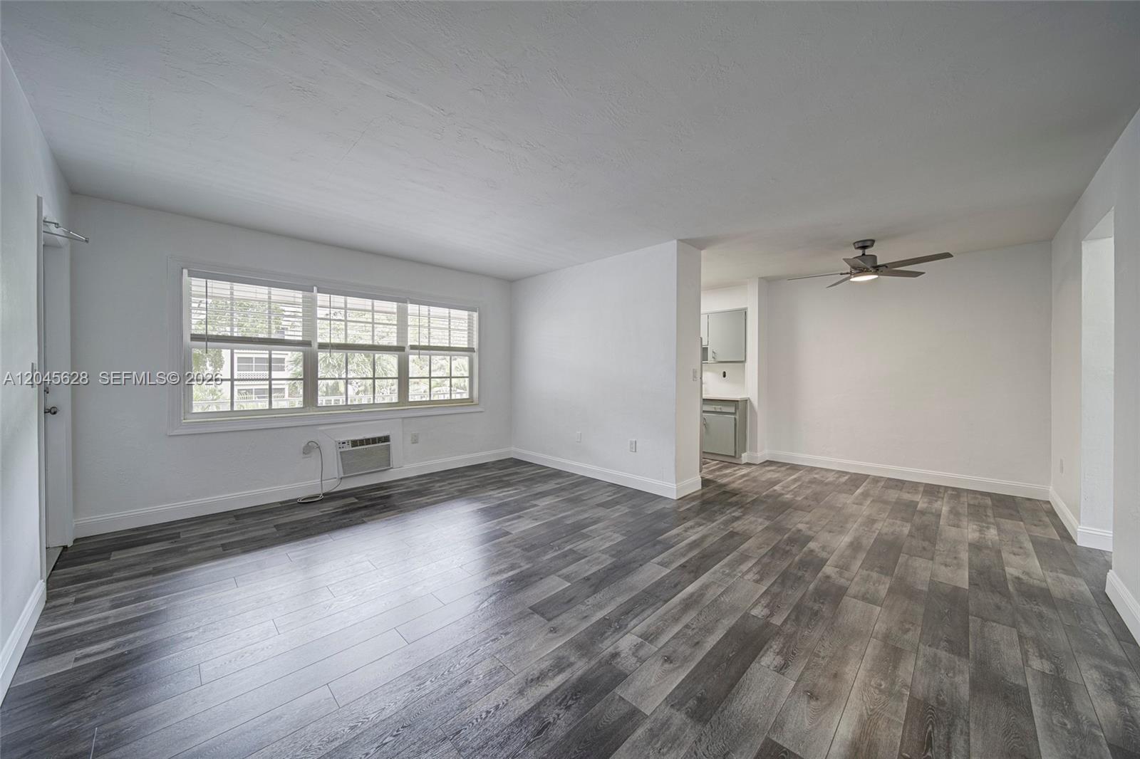 An empty living room features gray wood-look flooring, white walls, and a ceiling fan — 6565 Santona St # B19, Coral Gables FL 33146, CORAL GABLES, FL