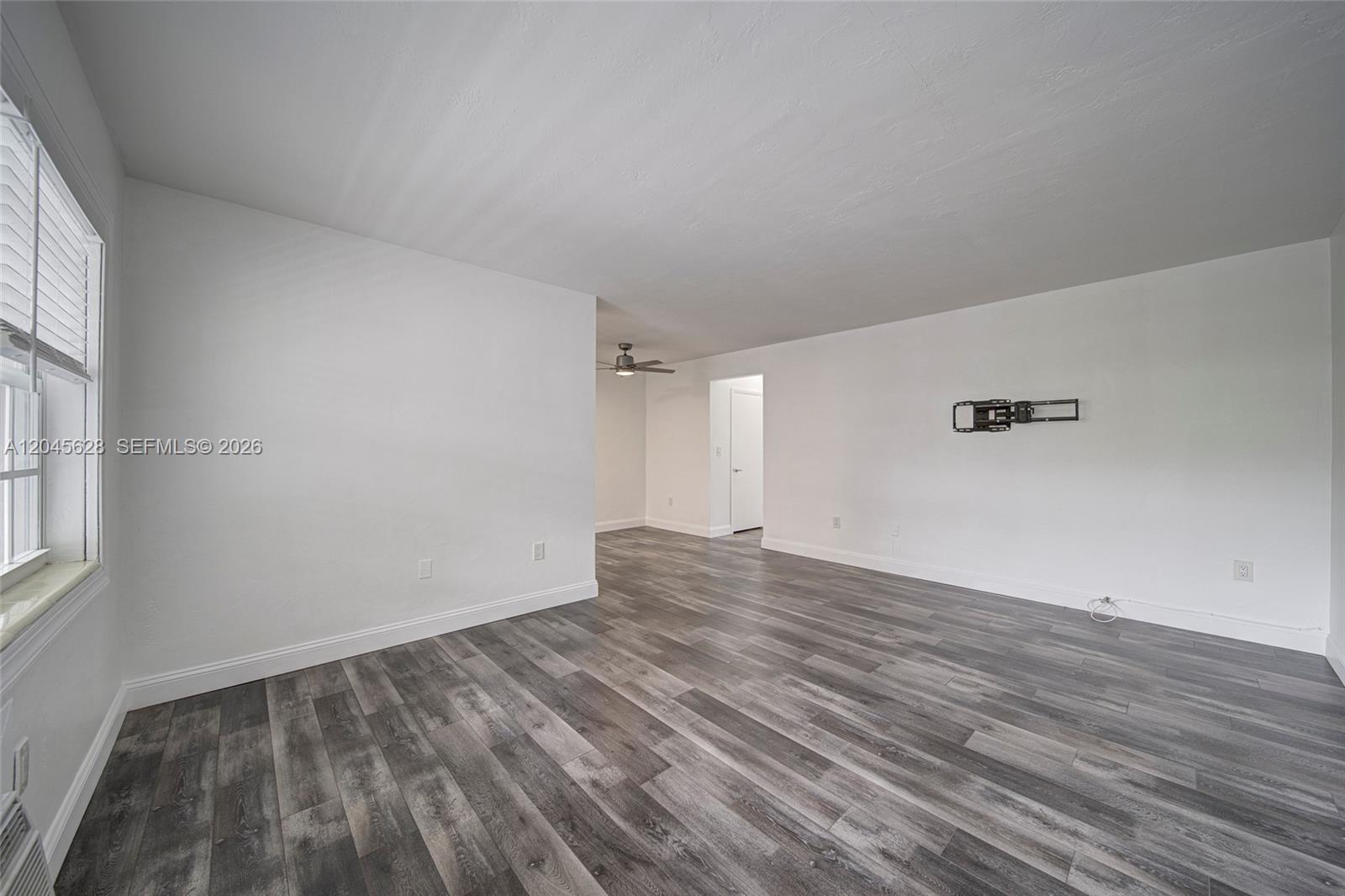 An empty room features white walls, gray wood-look flooring, and a wall-mounted television bracket — 6565 Santona St # B19, Coral Gables FL 33146, CORAL GABLES, FL