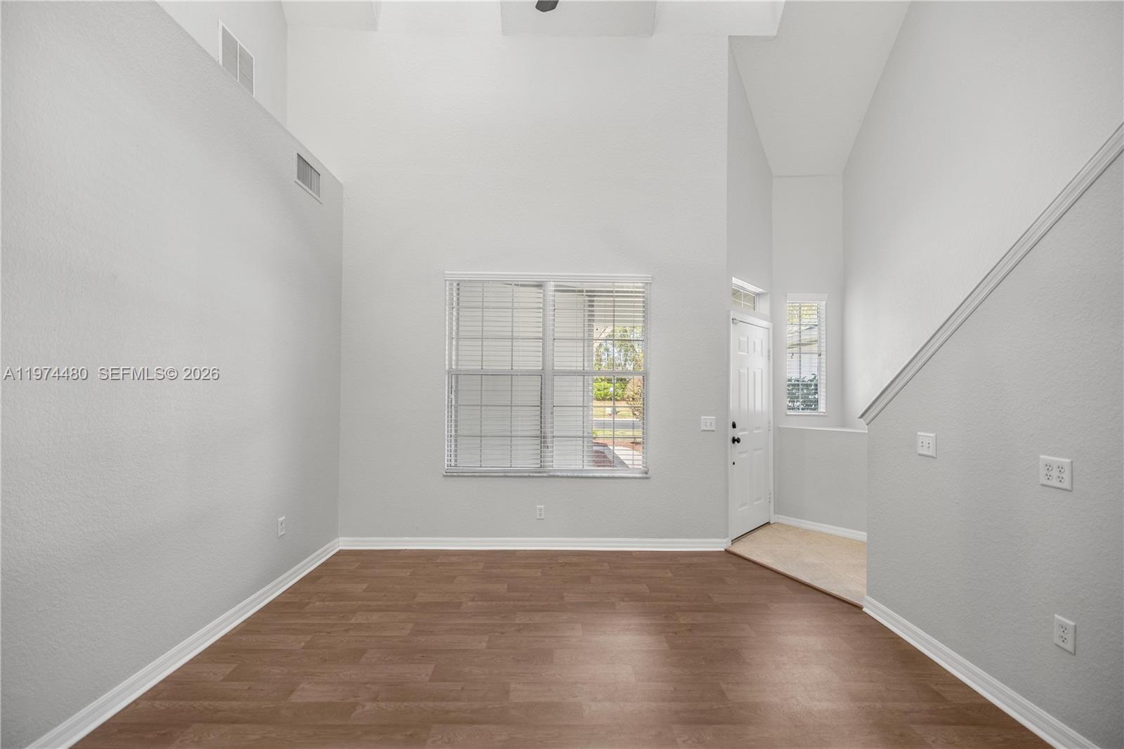 A bright, empty room features high ceilings, wood-look flooring, and a front entrance door — 231 NE 28th Ave Unit 103, Ocala FL 34470, OCALA, FL