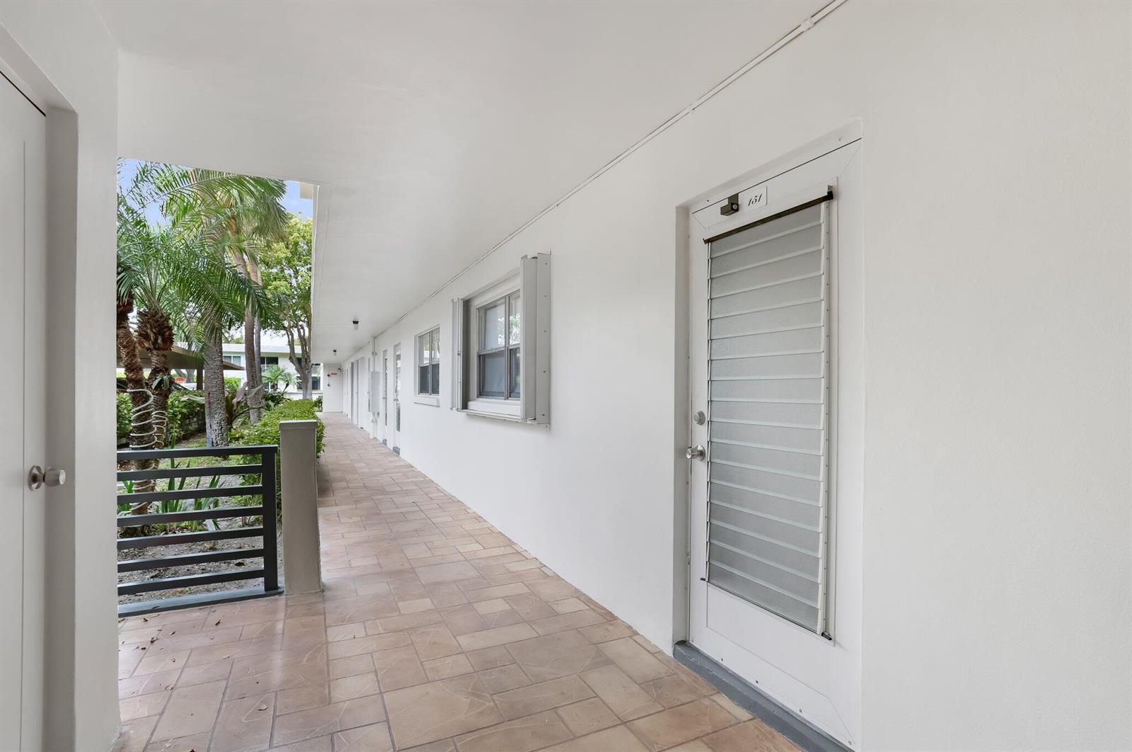A tiled outdoor walkway leads past a white door marked 151 and several windows — 3401 Spanish Trail # 151, Delray Beach FL 33483, DELRAY BEACH, FL