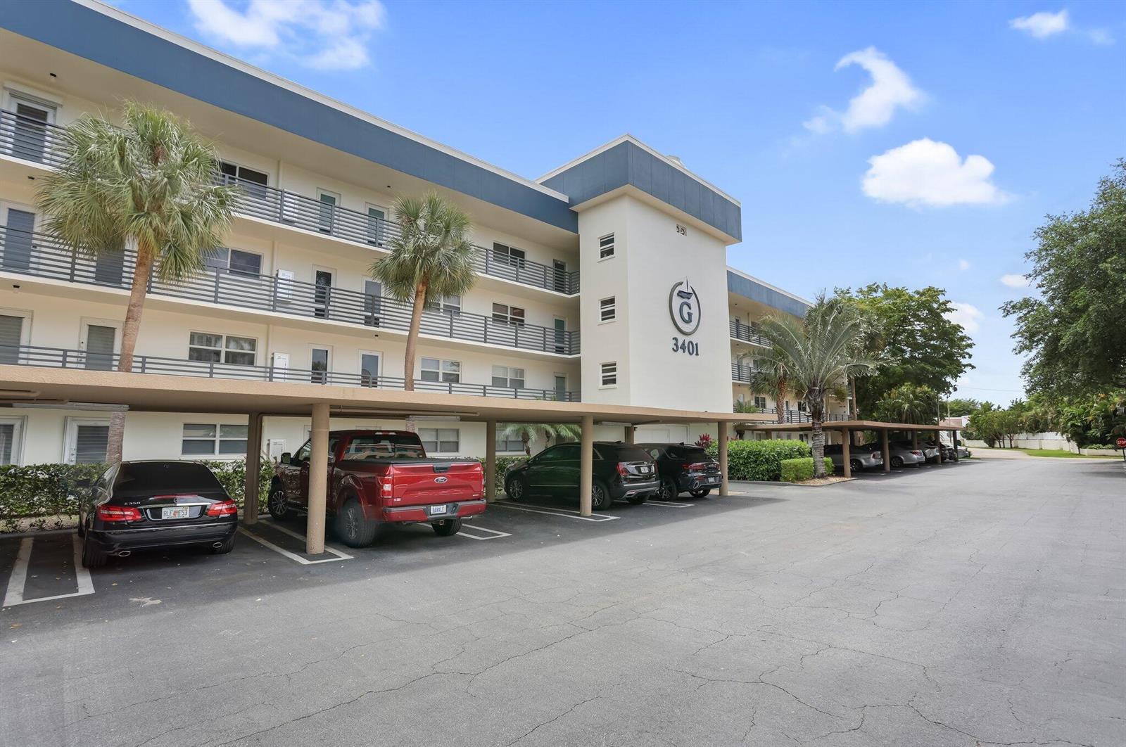 A multi-story apartment building with a covered parking area and several parked vehicles — 3401 Spanish Trail # 151, Delray Beach FL 33483, DELRAY BEACH, FL