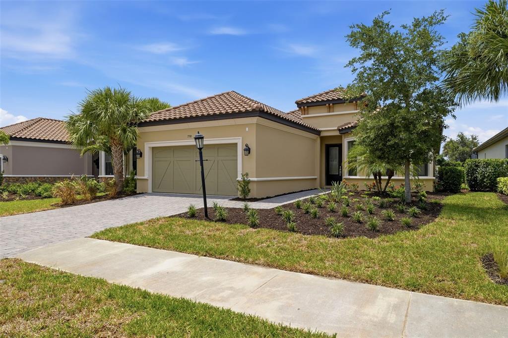 A single-story house with a tan stucco exterior, a tile roof, and a paved driveway — 7708 MOONBEAM AVENUE, SARASOTA, FL