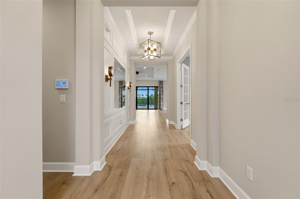 A hallway with light wood flooring, white wainscoting, a geometric chandelier, and a glass door — 7708 MOONBEAM AVENUE, SARASOTA, FL