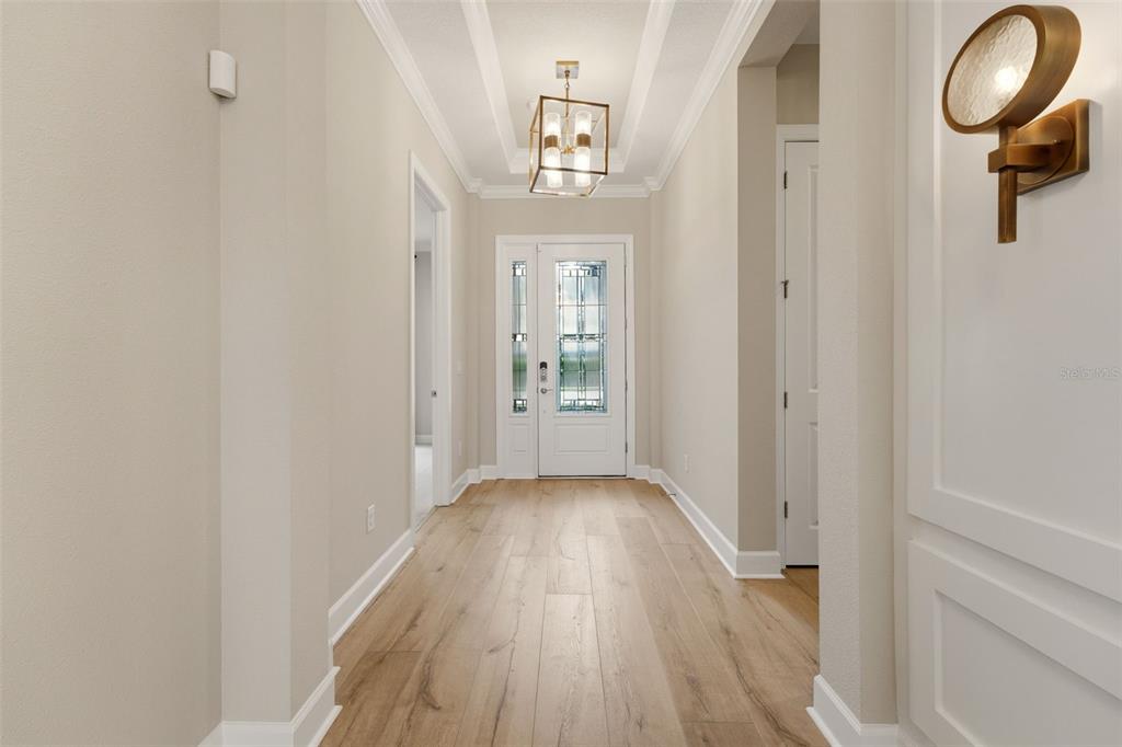A bright entryway features light wood flooring, a decorative ceiling fixture, and a white front door — 7708 MOONBEAM AVENUE, SARASOTA, FL