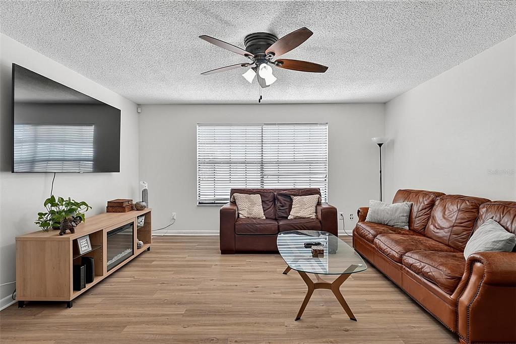 A living room features light wood flooring, a leather sofa, a television, and a ceiling fan — 9 BRIDGET TERRACE, ORMOND BEACH, FL
