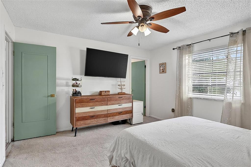 A bedroom features a wooden dresser, a wall-mounted television, and a green door — 9 BRIDGET TERRACE, ORMOND BEACH, FL