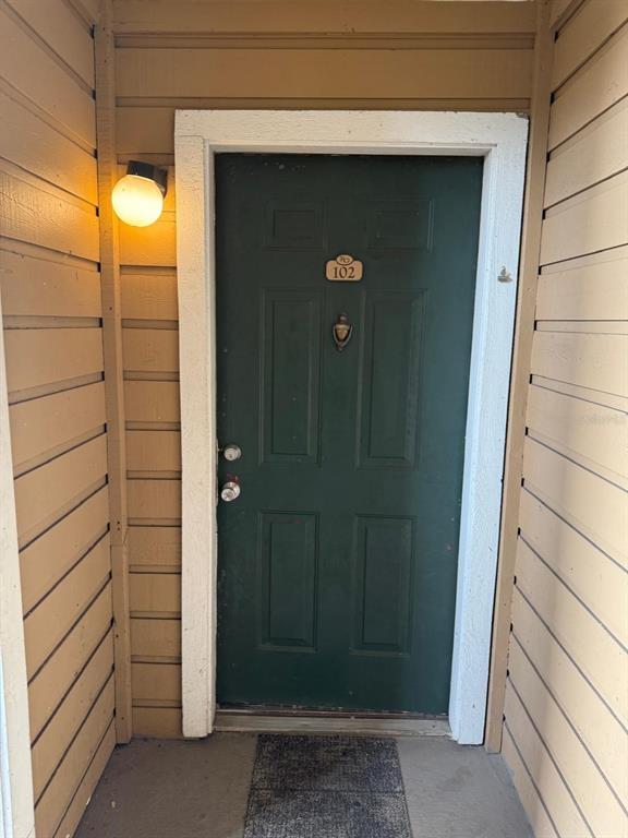 A dark green front door with the number 102 is set within tan horizontal siding — 4400 THORNBRIAR LANE UNIT 102, ORLANDO, FL