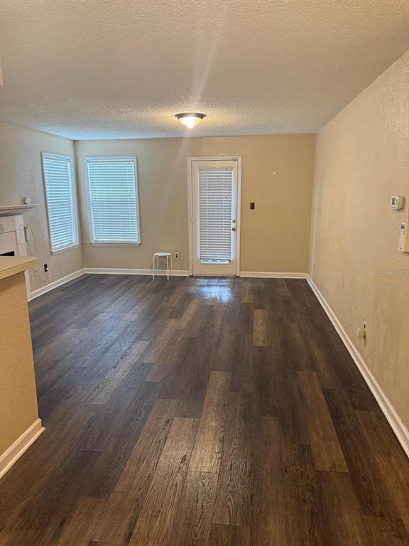 An empty living room features dark wood-look flooring, beige walls, two windows, and a door — 4400 THORNBRIAR LANE UNIT 102, ORLANDO, FL