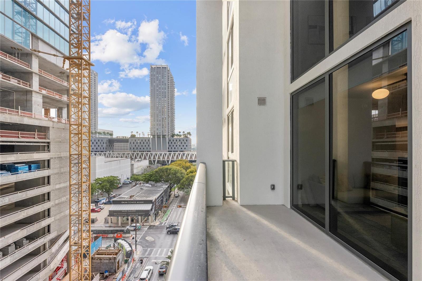A balcony overlooks a city street with a construction crane and nearby high-rise buildings — 11 NE 6th Street # 907, Miami FL 33132, MIAMI, FL