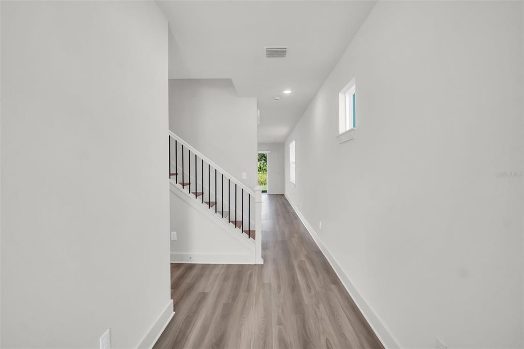 A hallway with light wood-look flooring, white walls, and a staircase with a black railing — 13718 HOMERIDGE COURT, HUDSON, FL