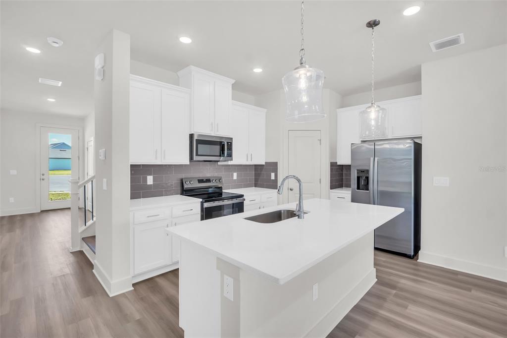 A modern kitchen features white cabinets, a central island with a sink, and stainless appliances — 13718 HOMERIDGE COURT, HUDSON, FL