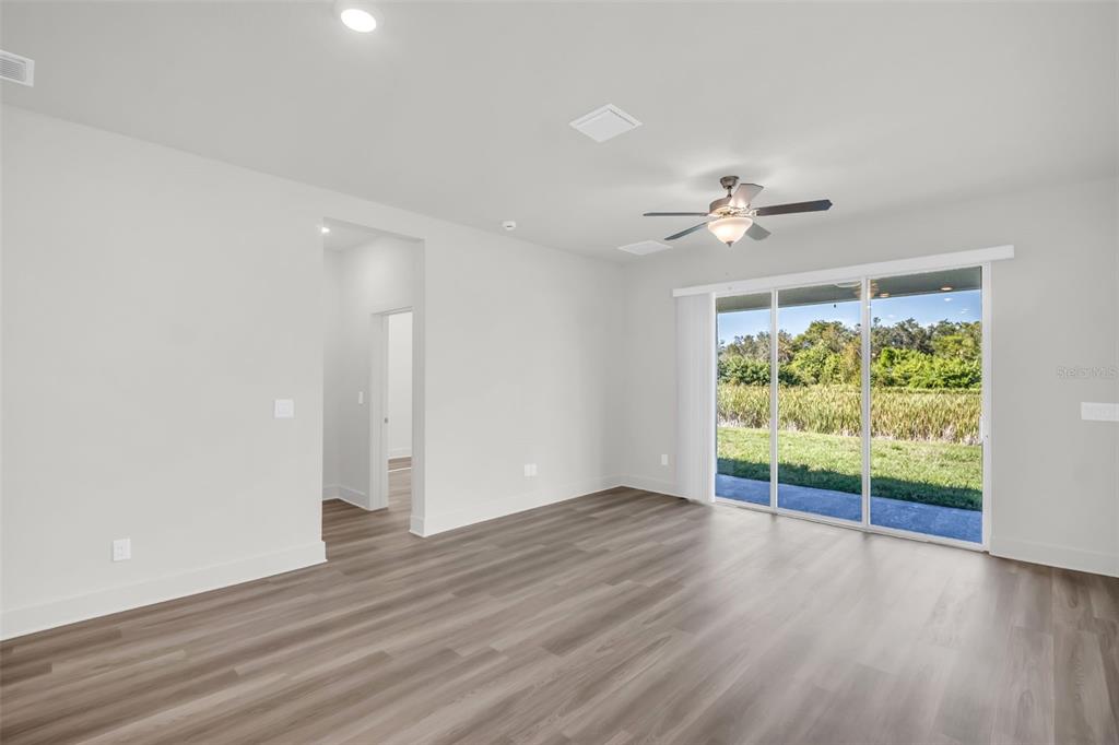 A bright living room features light gray walls, wood-look flooring, a ceiling fan, and sliding doors — 13718 HOMERIDGE COURT, HUDSON, FL