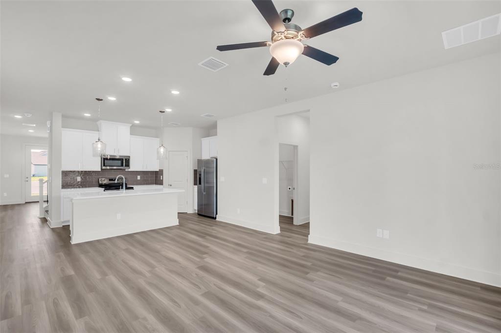 An open-concept kitchen and living area feature white cabinetry, stainless steel appliances, and wood-look flooring — 13718 HOMERIDGE COURT, HUDSON, FL