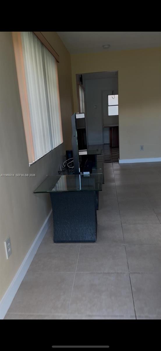 A room with light-colored tile flooring, a glass-topped television stand, and vertical window blinds — 18 SW 13th St, Dania Beach FL 33004, DANIA BEACH, FL