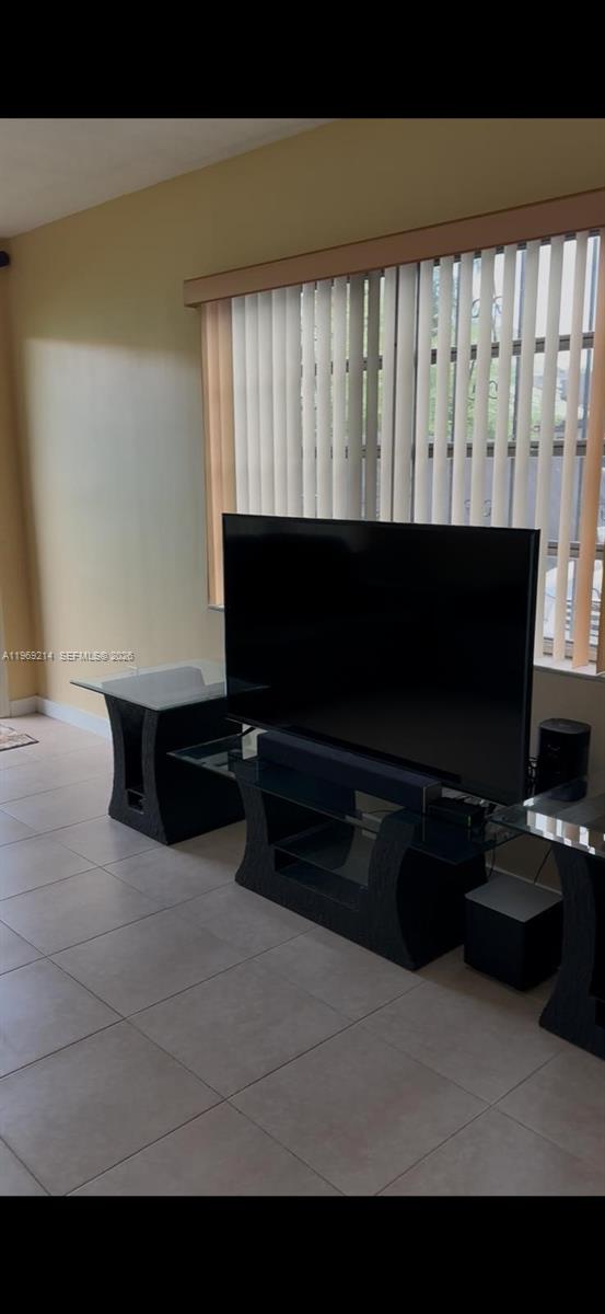 A living room features a black television on a glass stand in front of vertical blinds — 18 SW 13th St, Dania Beach FL 33004, DANIA BEACH, FL