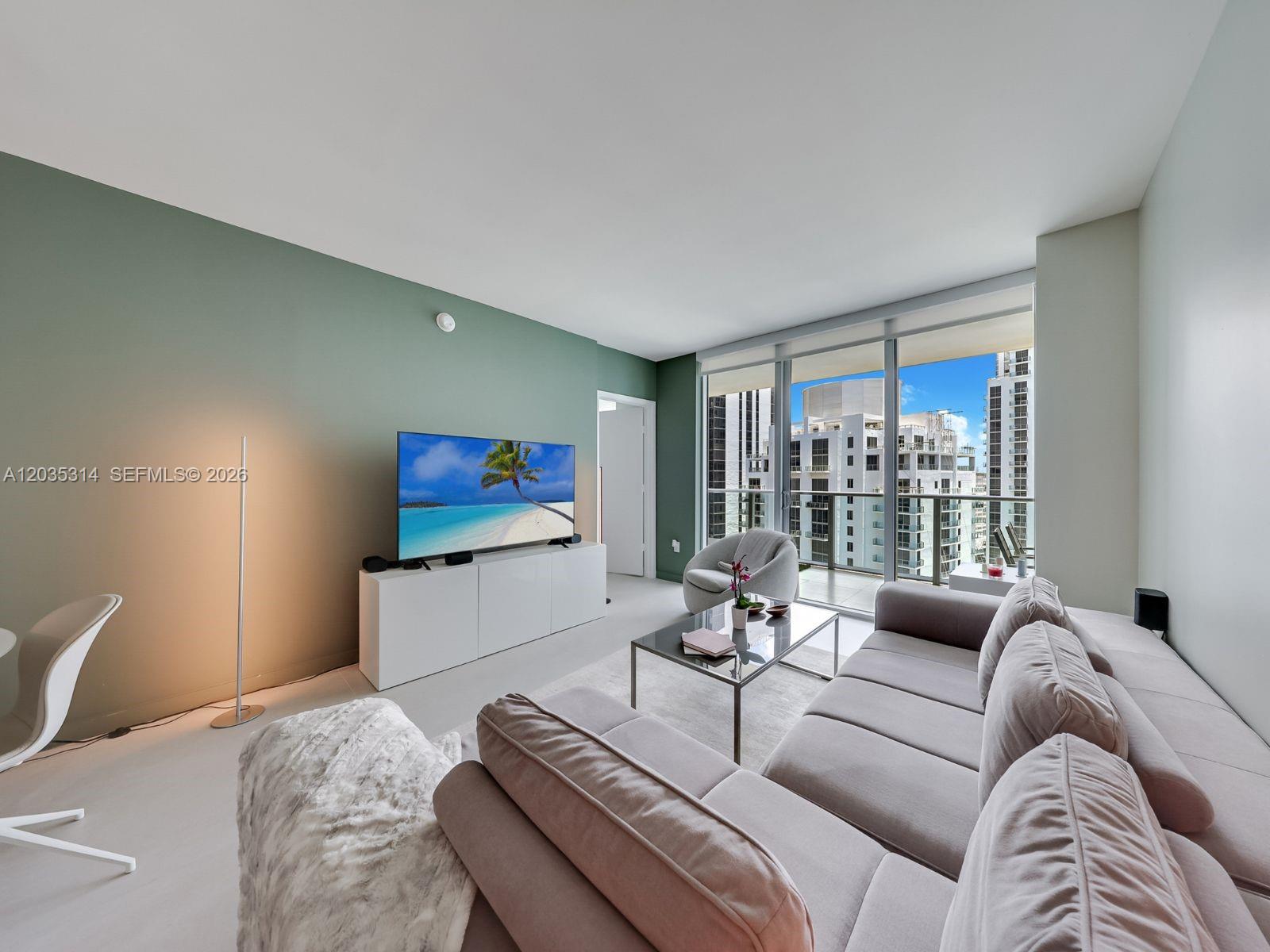 A living room features a green accent wall, a large sofa, and floor-to-ceiling windows — 1100 S Miami Ave # 3411, Miami FL 33130, MIAMI, FL