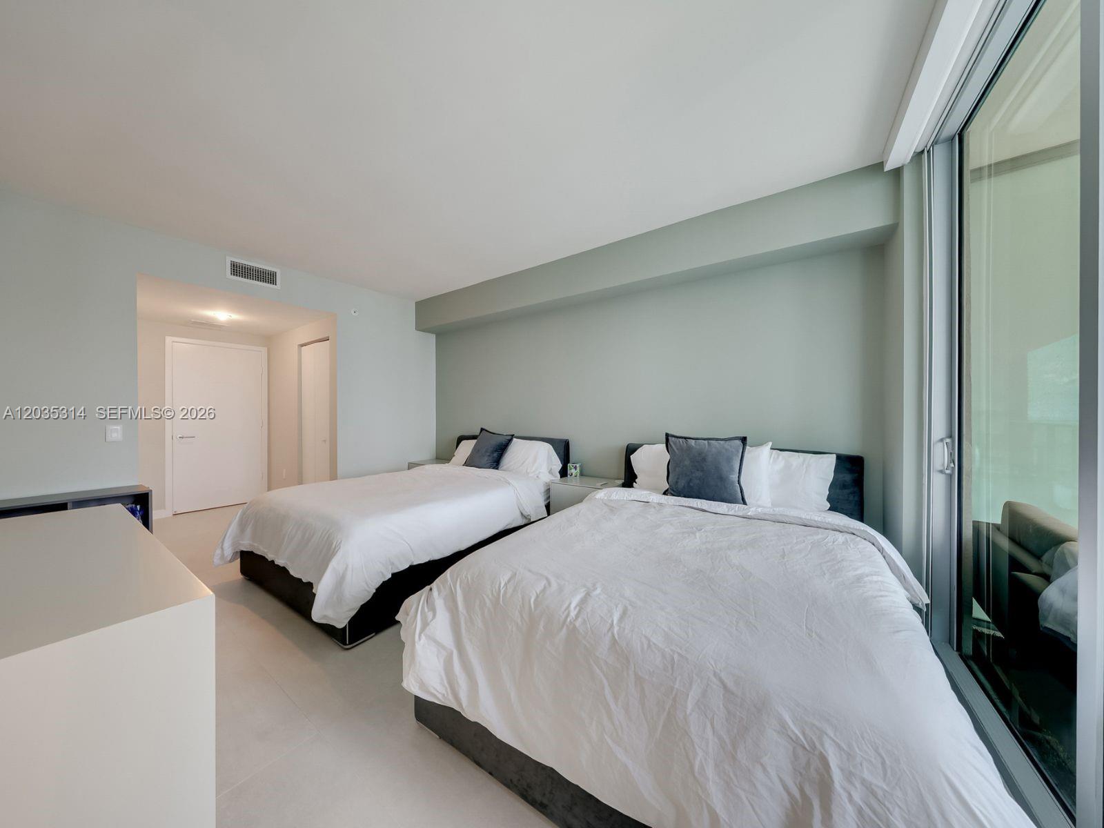 A bedroom features two beds, light-colored walls, tile flooring, and a large sliding glass door — 1100 S Miami Ave # 3411, Miami FL 33130, MIAMI, FL